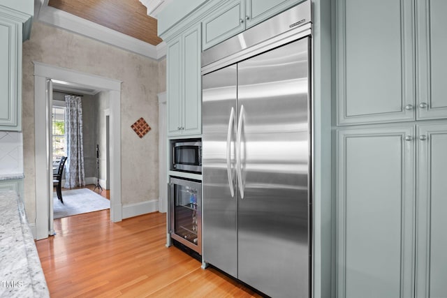 kitchen featuring built in appliances, wine cooler, baseboards, light stone counters, and light wood-style flooring
