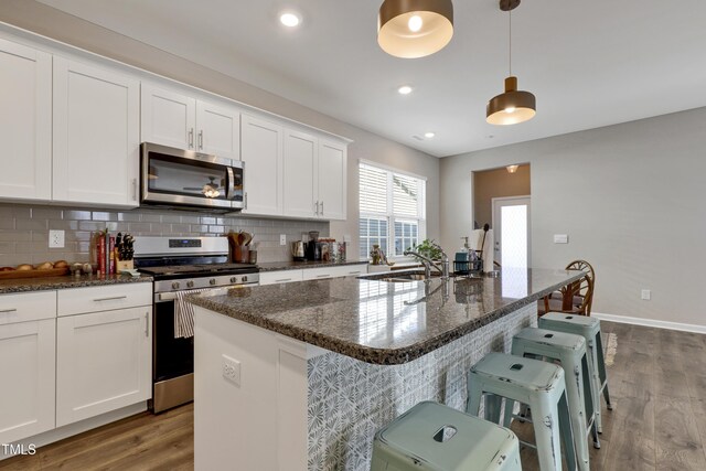 kitchen featuring appliances with stainless steel finishes, a sink, white cabinets, dark wood-style floors, and an island with sink