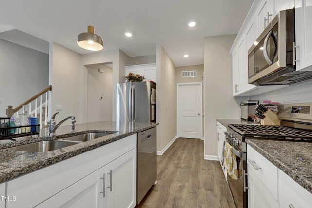kitchen featuring visible vents, appliances with stainless steel finishes, light wood-type flooring, a sink, and dark stone countertops
