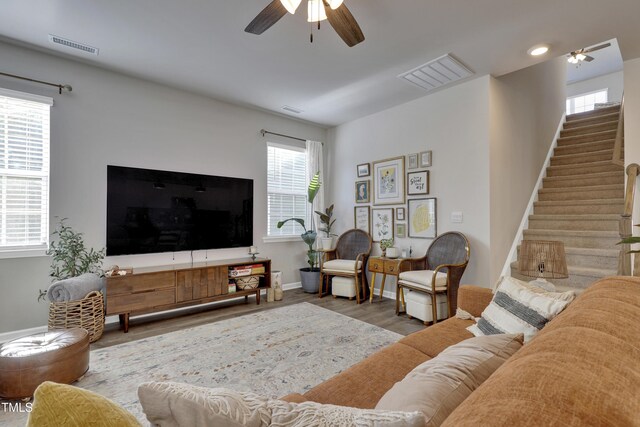 living room featuring visible vents, a ceiling fan, stairs, and wood finished floors
