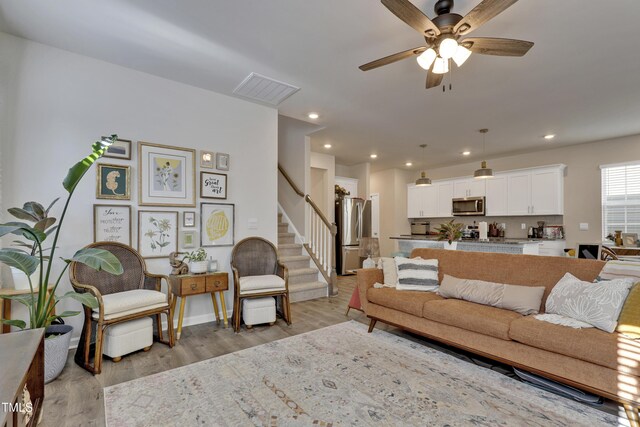 living room featuring ceiling fan, light wood-style flooring, recessed lighting, visible vents, and stairway