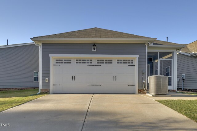 view of front of home with an attached garage, central AC unit, a shingled roof, and concrete driveway