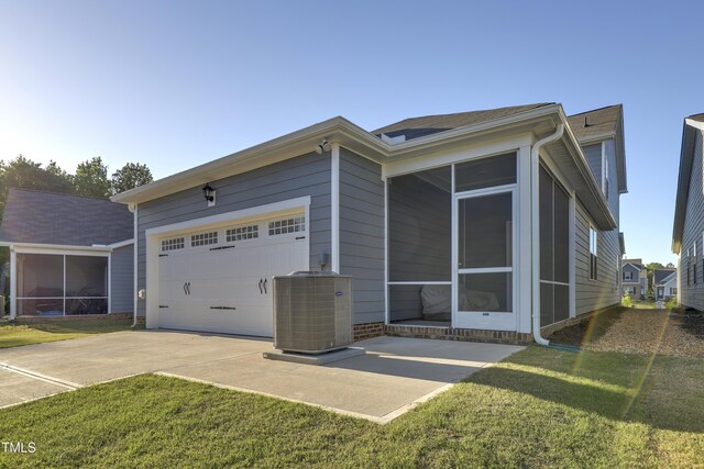 exterior space with an attached garage, central AC, a sunroom, concrete driveway, and a yard