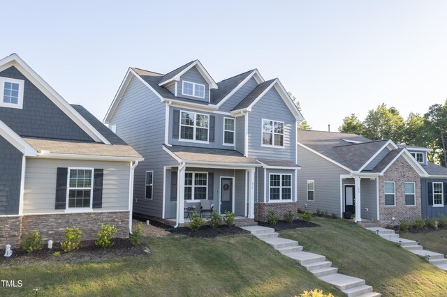 craftsman inspired home with a porch, stone siding, and a front lawn