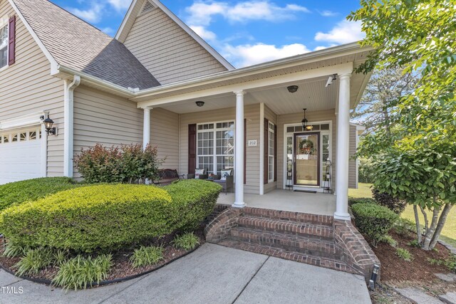 view of exterior entry featuring a porch, a shingled roof, and a garage