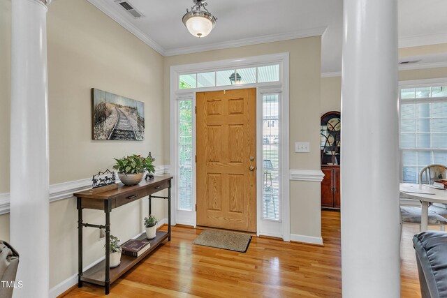 foyer entrance featuring visible vents, crown molding, decorative columns, wood finished floors, and baseboards