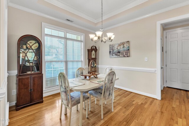 dining area featuring crown molding, a raised ceiling, light wood-style flooring, and a notable chandelier