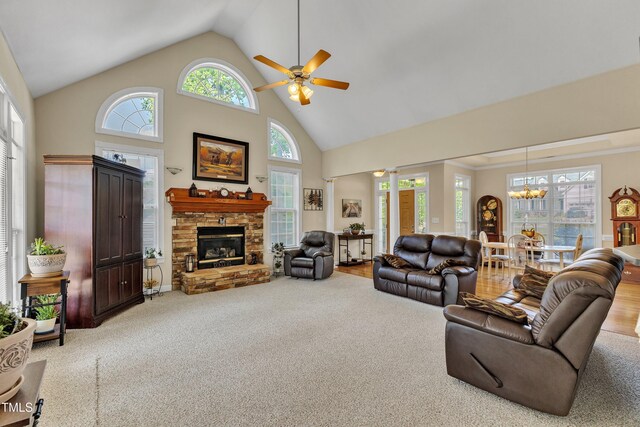 carpeted living area featuring high vaulted ceiling, a stone fireplace, and ceiling fan with notable chandelier
