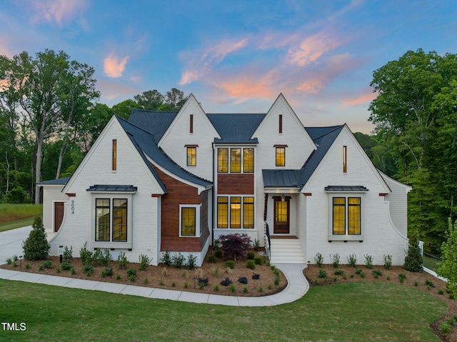 modern inspired farmhouse with a lawn, metal roof, brick siding, and a standing seam roof