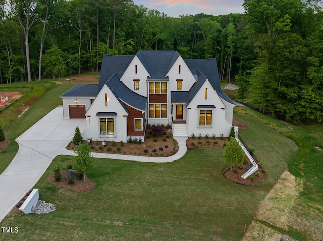 modern farmhouse style home featuring a garage, a yard, driveway, and a forest view