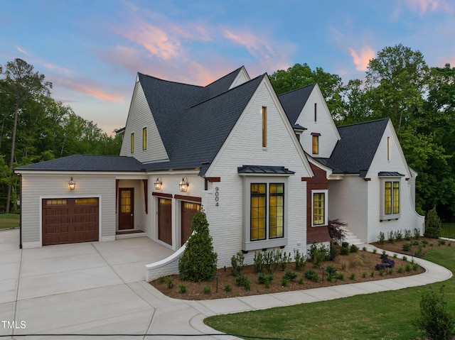 modern farmhouse with an attached garage, a shingled roof, brick siding, and concrete driveway