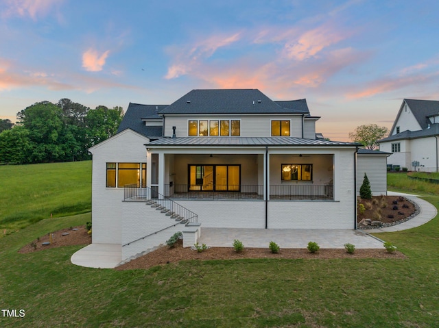 rear view of house with ceiling fan, a standing seam roof, brick siding, a patio area, and a lawn