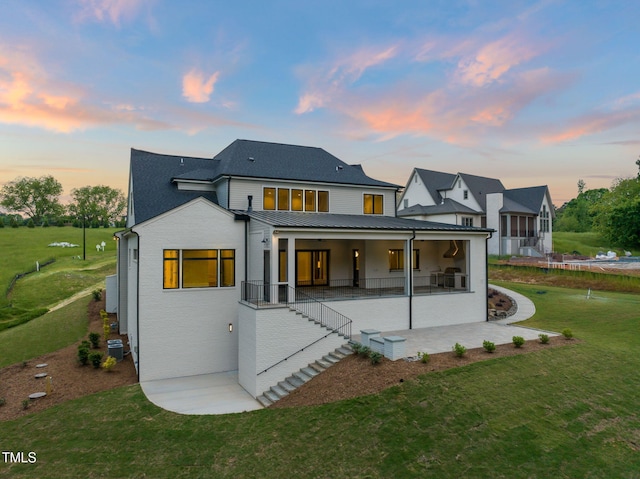 back of property at dusk with a standing seam roof, metal roof, central AC unit, a yard, and a patio