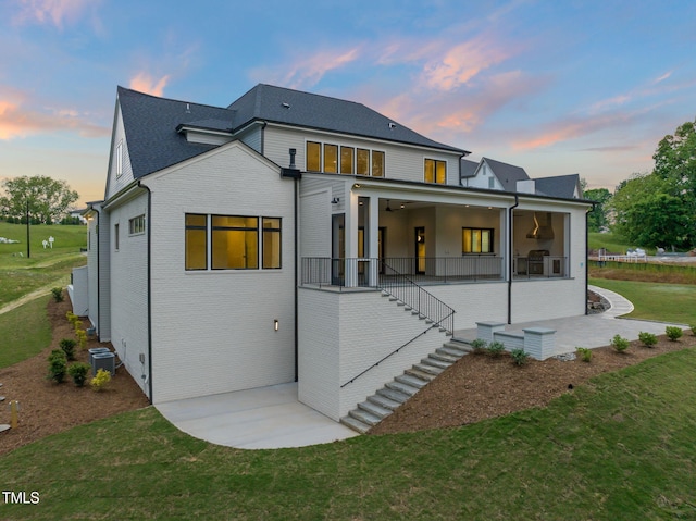 back of house featuring brick siding, stairway, a patio area, central air condition unit, and a lawn