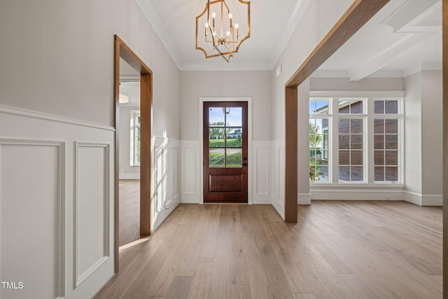 entryway featuring ornamental molding, a decorative wall, light wood-type flooring, a wainscoted wall, and a chandelier