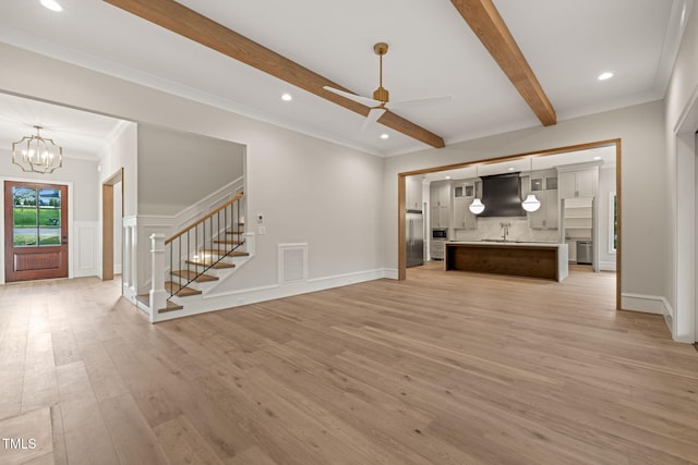 unfurnished living room with visible vents, beamed ceiling, ceiling fan with notable chandelier, light wood finished floors, and stairs
