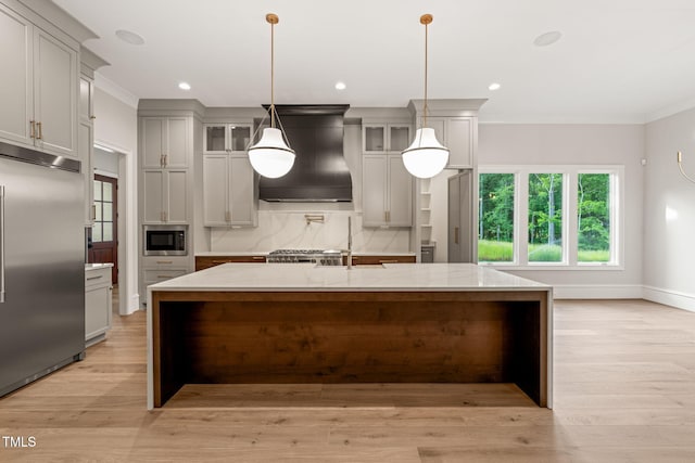 kitchen with built in appliances, ornamental molding, custom range hood, and a large island with sink