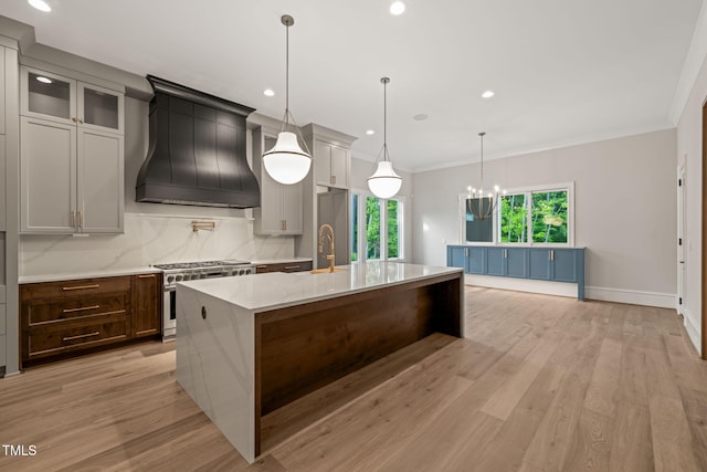 kitchen featuring stainless steel range, an island with sink, premium range hood, recessed lighting, and tasteful backsplash