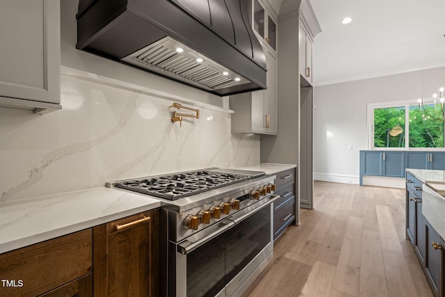 kitchen with glass insert cabinets, premium range hood, light stone counters, light wood finished floors, and double oven range