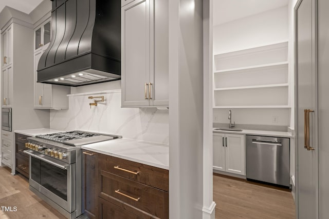kitchen with stainless steel appliances, a sink, custom range hood, and light wood-style floors