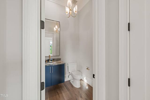 bathroom featuring wood finished floors, vanity, baseboards, toilet, and an inviting chandelier