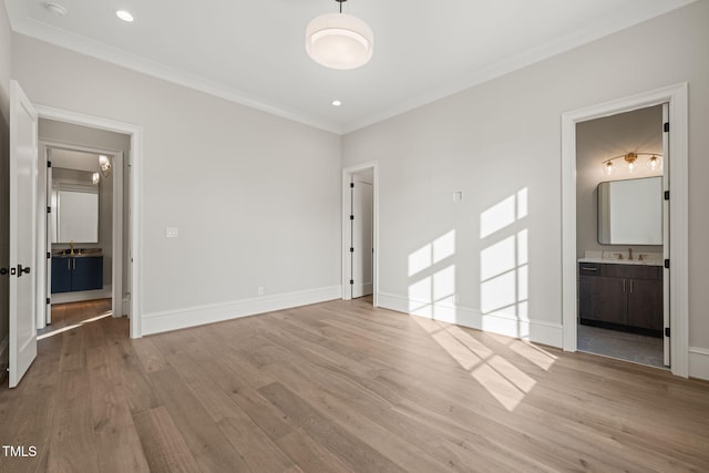 unfurnished bedroom with crown molding, a sink, ensuite bath, baseboards, and wood finished floors