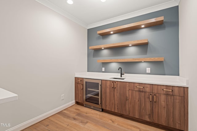 bar with ornamental molding, wine cooler, light wood-style floors, a sink, and wet bar