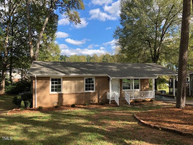 ranch-style home with a porch, brick siding, a front lawn, and a carport