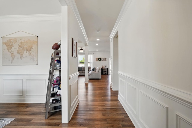 hallway with ornamental molding, wainscoting, a decorative wall, and dark wood-style floors
