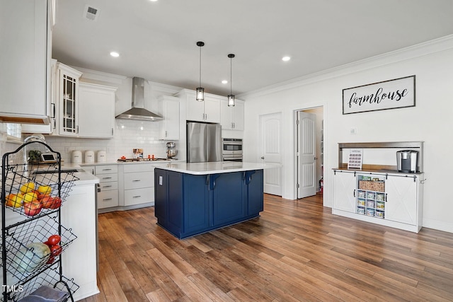 kitchen featuring visible vents, wall chimney range hood, appliances with stainless steel finishes, backsplash, and blue cabinetry