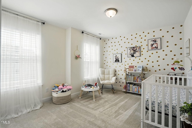 carpeted bedroom featuring a nursery area and baseboards