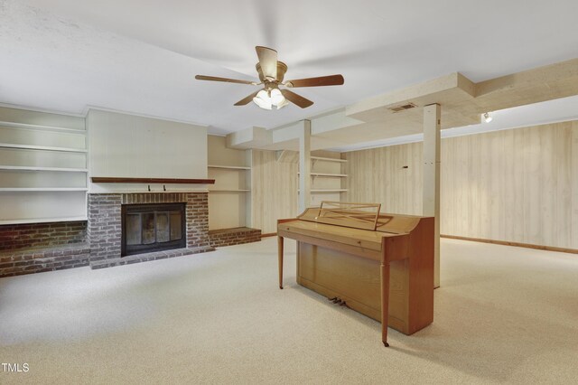 carpeted living area with a brick fireplace, wood walls, built in shelves, a ceiling fan, and visible vents