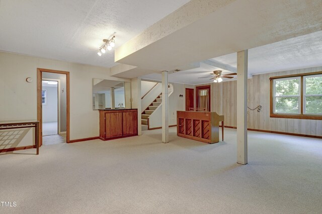 unfurnished living room featuring ceiling fan, a textured ceiling, carpet, stairs, and baseboards