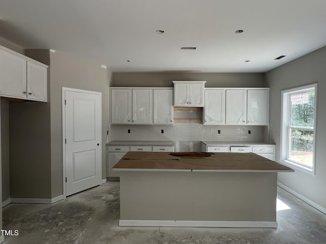 169 Pecan Valley Way, Four Oaks, NC 27524 - kitchen featuring a kitchen island, concrete flooring, decorative backsplash, baseboards, and white cabinets