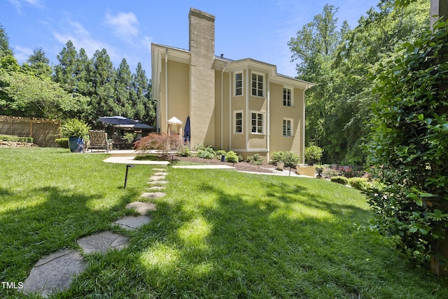 back of property featuring stucco siding, a yard, a chimney, and fence