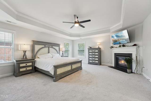 bedroom with visible vents, crown molding, a fireplace with flush hearth, baseboards, and a tray ceiling