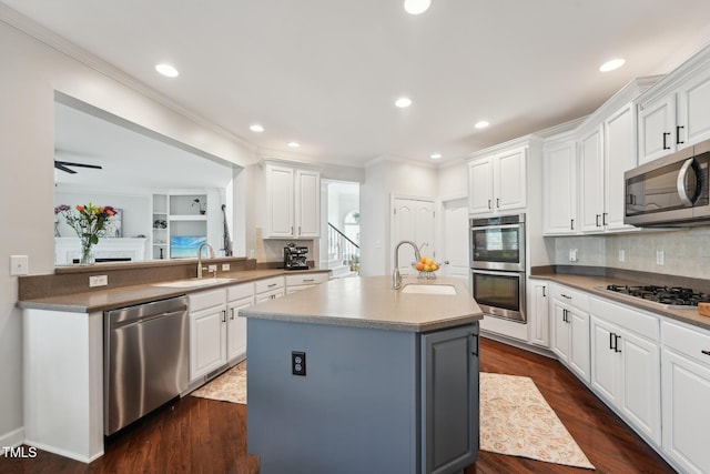 kitchen featuring stainless steel appliances, ornamental molding, a center island with sink, and a sink