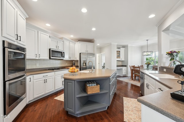 kitchen featuring open shelves, an island with sink, gray cabinets, a sink, and appliances with stainless steel finishes
