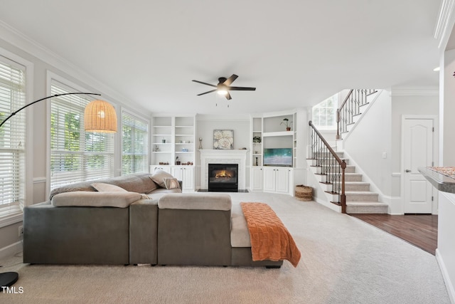 living area featuring a glass covered fireplace, ornamental molding, stairway, and a ceiling fan