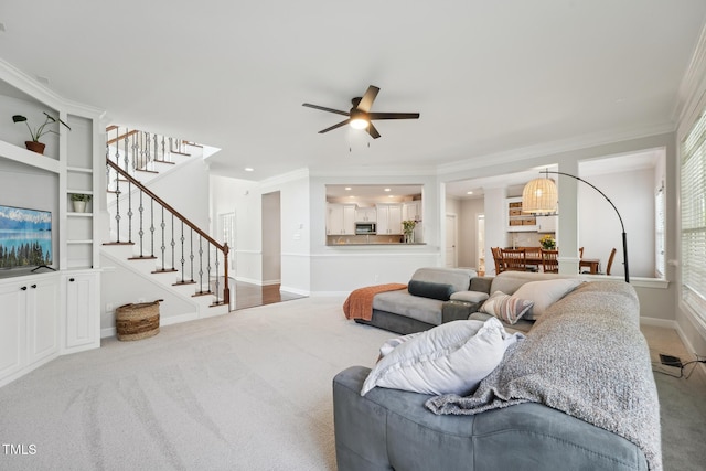carpeted living room featuring baseboards, ornamental molding, stairs, and ceiling fan