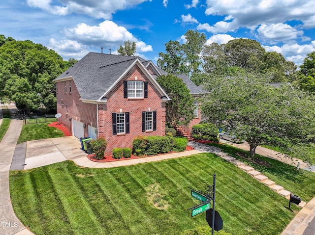 traditional-style home featuring roof with shingles, a front lawn, brick siding, a garage, and driveway