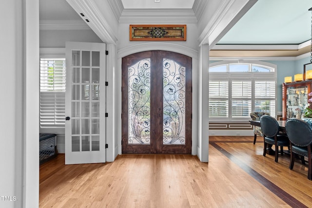 foyer entrance with french doors, ornamental molding, wood finished floors, and a healthy amount of sunlight