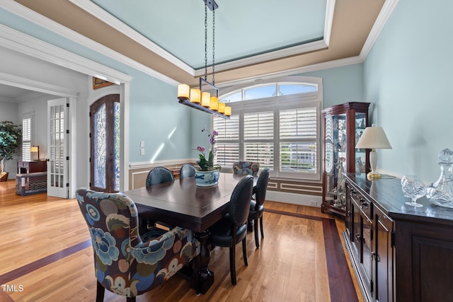 dining area with light wood-style floors, ornamental molding, and a wainscoted wall