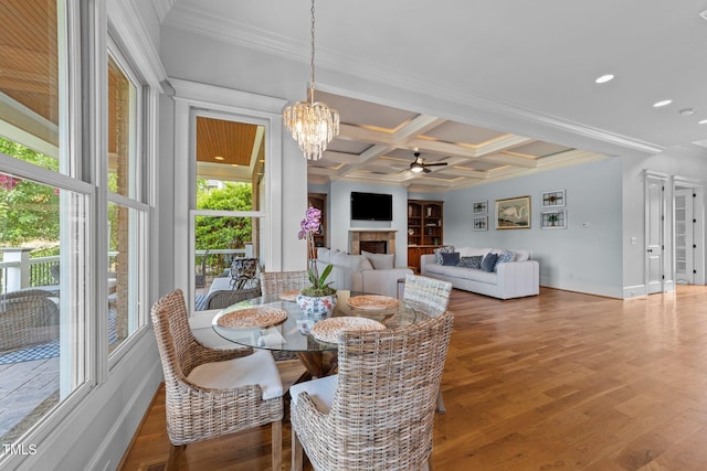 dining area with ornamental molding, a fireplace, beamed ceiling, coffered ceiling, and ceiling fan with notable chandelier