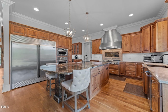 kitchen with brown cabinetry, wall chimney exhaust hood, and appliances with stainless steel finishes