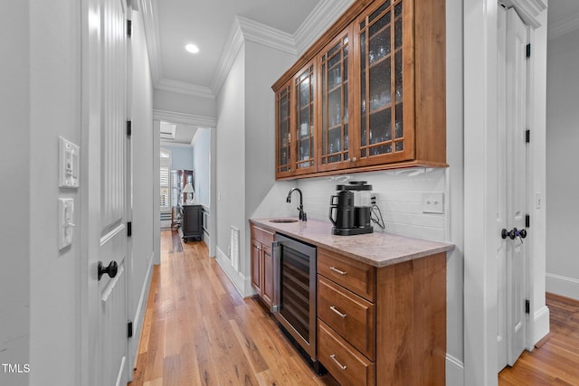 bar with ornamental molding, beverage cooler, baseboards, a sink, and light wood-style flooring