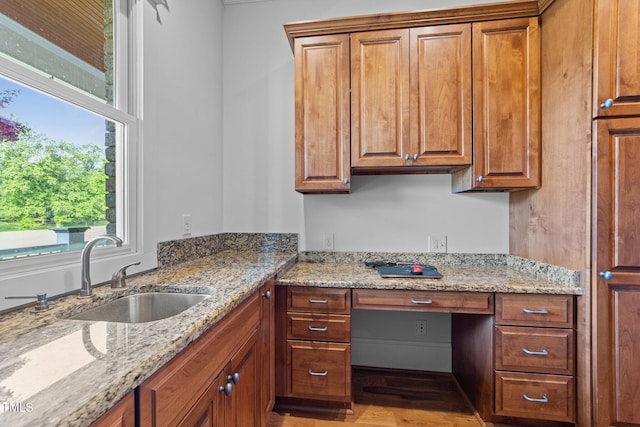 kitchen with brown cabinets, light stone counters, and a sink