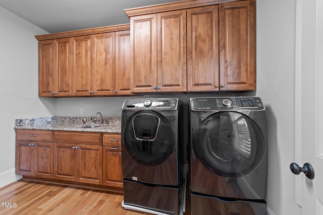 clothes washing area featuring washer and dryer, light wood-style floors, baseboards, a sink, and cabinet space