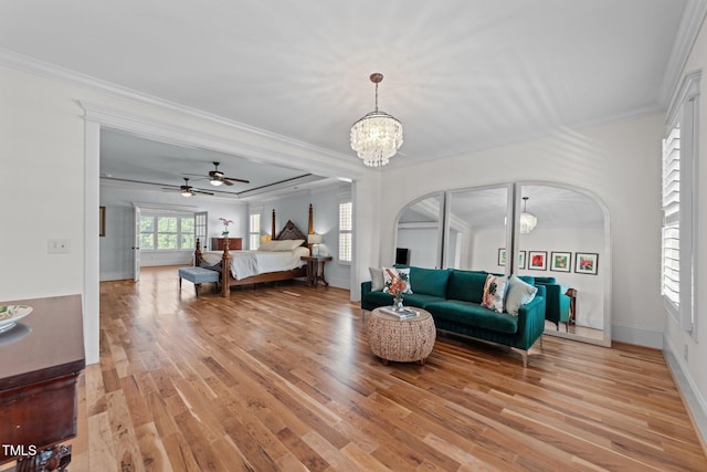 living room with arched walkways, ornamental molding, ceiling fan with notable chandelier, and light wood-style flooring