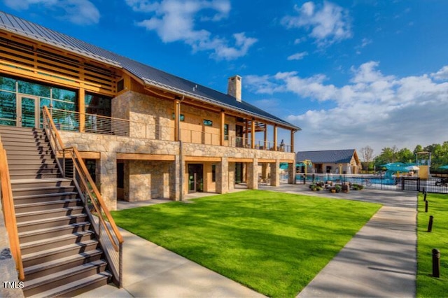 rear view of house with stairway, a chimney, an outdoor pool, and stone siding
